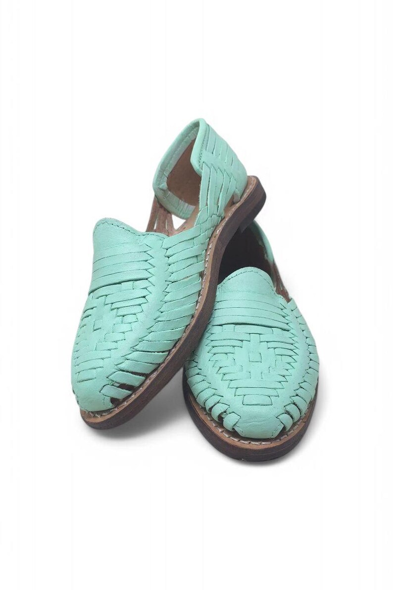May include: A pair of mint green huarache sandals. The sandals have a woven leather design and a brown sole. The open-toe shoes are displayed on a white background. These sandals are a summer footwear option.