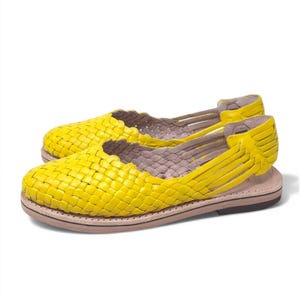 May include: A pair of yellow woven leather sandals with a flat sole.