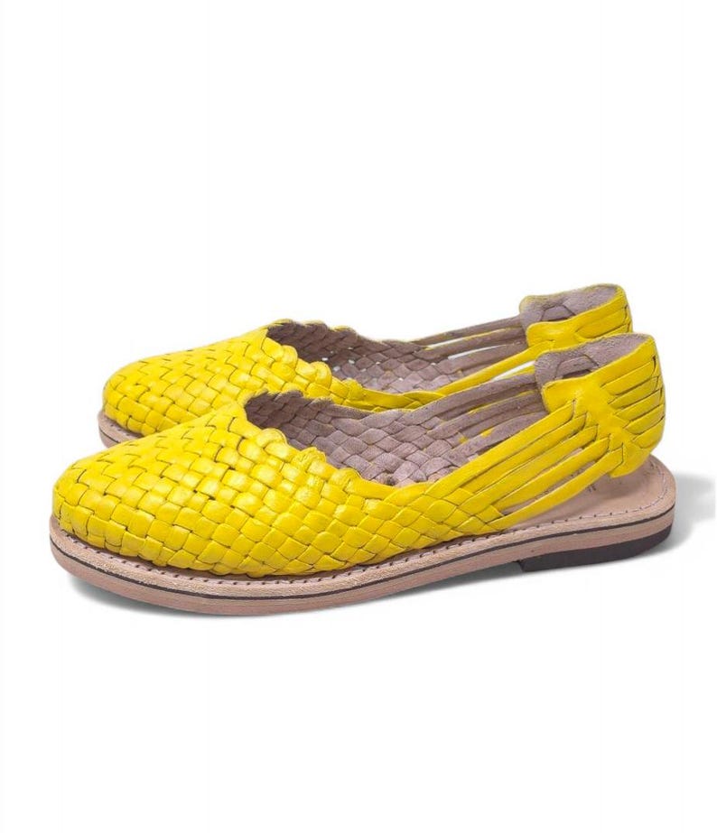 May include: A pair of yellow woven leather sandals with a flat sole.