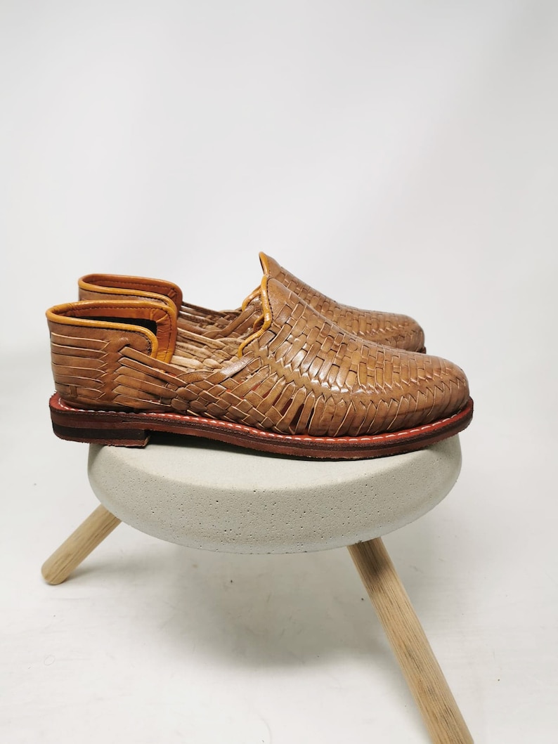 May include: A pair of woven leather sandals in a light brown color. The sandals have a simple design and are made of a soft, supple leather. They are perfect for casual wear and would be comfortable for everyday use.
