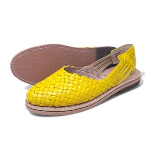 May include: Yellow leather sandals with a woven design. The sandals have a strap that goes around the ankle and a closed toe.