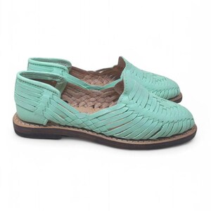 May include: A pair of mint green leather huarache sandals. The sandals have a woven design across the top and a brown sole. The open-toe shoes have a low heel and are designed for casual wear.