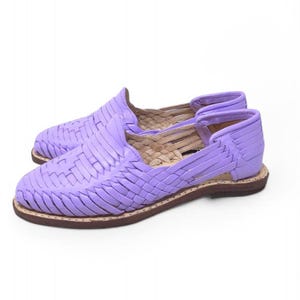 May include: A pair of lavender huarache sandals. These woven leather shoes have a closed toe and heel with an open side design. The soles are brown with a light-colored stitching.