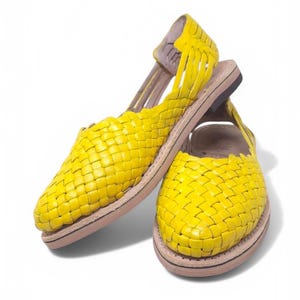 May include: A pair of yellow woven leather sandals with a closed toe and an open heel. The sandals have a simple design and are made of a soft, comfortable material.