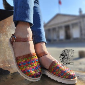 Puede incluir: Sandalias de cuero tejido con un patr&oacute;n geom&eacute;trico colorido. Las sandalias tienen una correa de tobillo de cuero marr&oacute;n con hebilla y suela blanca. La imagen incluye el texto "D'Lolos".