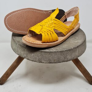 May include: Yellow leather sandals with a woven design. The sandals have a strap that goes around the ankle and a toe loop.