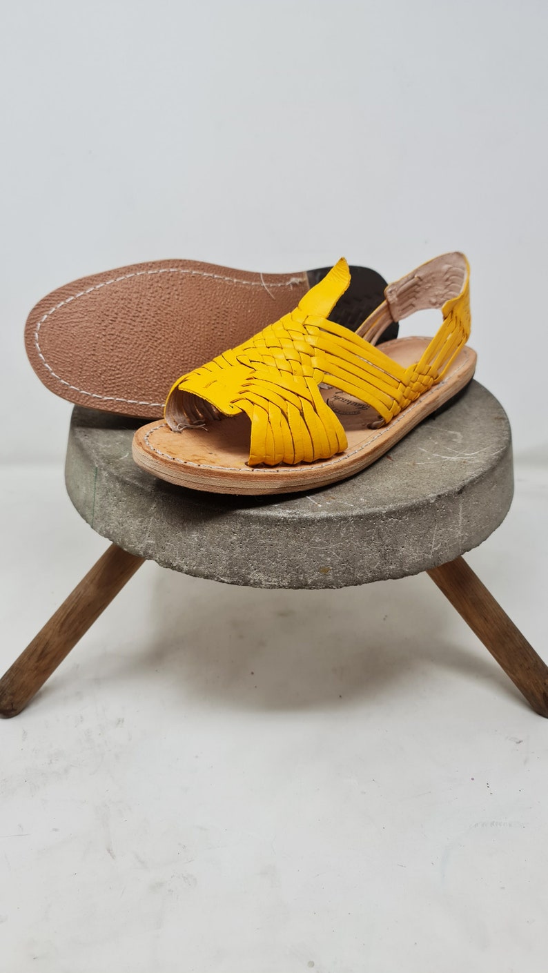 May include: Yellow leather sandals with a woven design. The sandals have a strap that goes around the ankle and a toe loop.