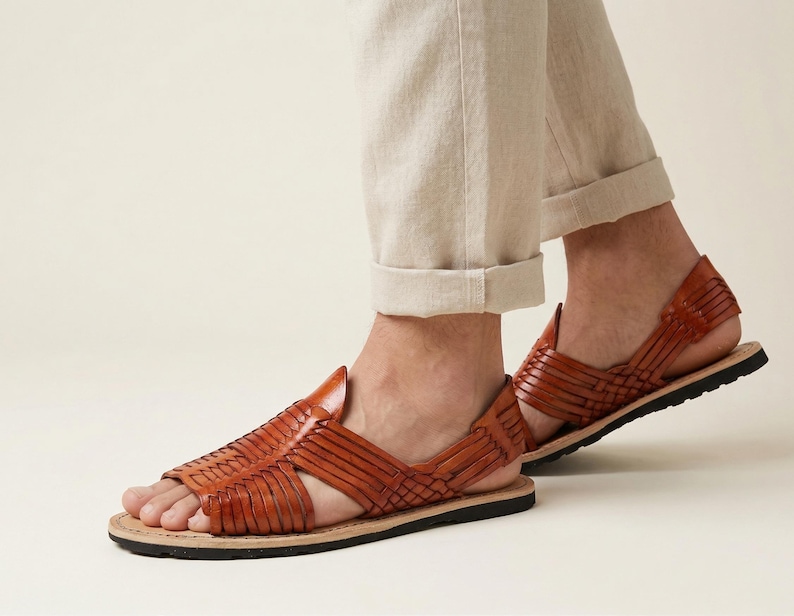 May include: Brown leather sandals with a woven design. The sandals have a flat sole and a strap around the ankle. The sandals are worn with beige trousers. The sandals are a size 9.