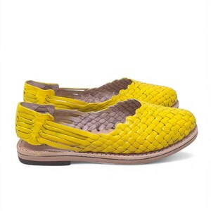 May include: A pair of yellow woven leather sandals with a flat sole. The sandals have a criss-cross design and are open-toed.