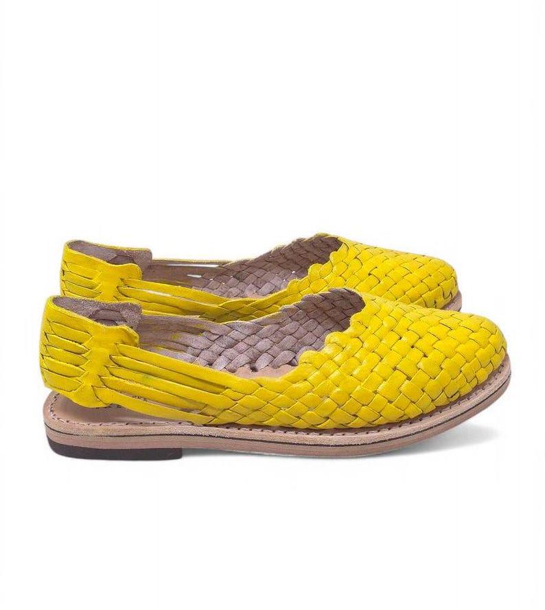May include: A pair of yellow woven leather sandals with a flat sole. The sandals have a criss-cross design and are open-toed.