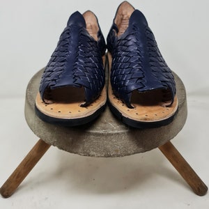 Pu&ograve; includere: Un paio di sandali in pelle blu navy con un design intrecciato. I sandali hanno una punta aperta e una suola piatta.