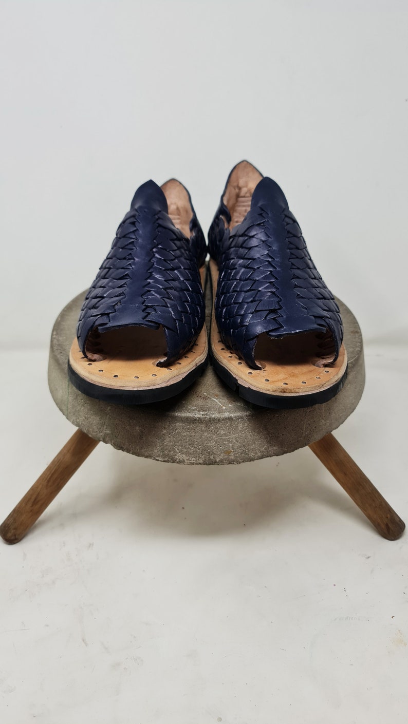 Pu&ograve; includere: Un paio di sandali in pelle blu navy con un design intrecciato. I sandali hanno una punta aperta e una suola piatta.