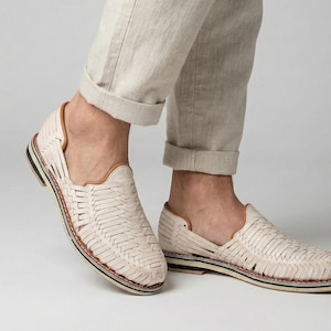 May include: Cream-colored woven leather shoes with a low profile. The shoes have a woven design, a brown leather trim, and a black and white sole. The shoes are worn with beige pants.