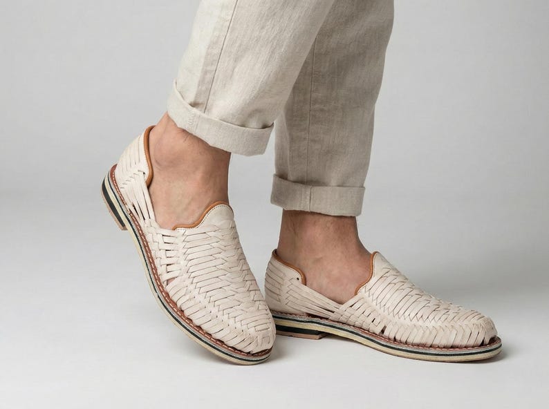 May include: Cream-colored woven leather shoes with a low profile. The shoes have a woven design, a brown leather trim, and a black and white sole. The shoes are worn with beige pants.
