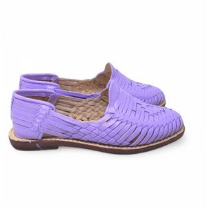 May include: A pair of lavender huarache sandals. These woven leather shoes have a flat sole and a closed toe design. The sandals are a light purple color with a brown sole.
