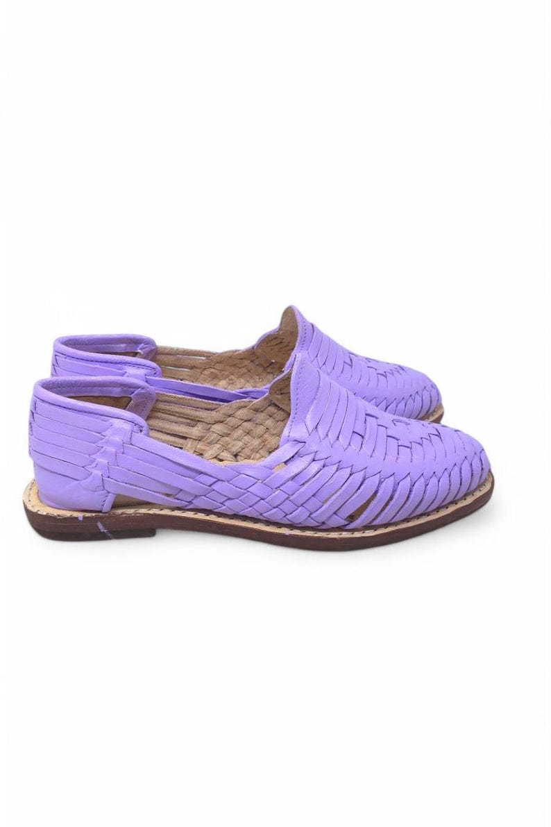 May include: A pair of lavender huarache sandals. These woven leather shoes have a flat sole and a closed toe design. The sandals are a light purple color with a brown sole.