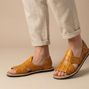 May include: Mustard yellow leather sandals with woven straps. The sandals have a black sole and a natural-coloured insole. The open-toe design and woven pattern provide a stylish and breathable footwear option.