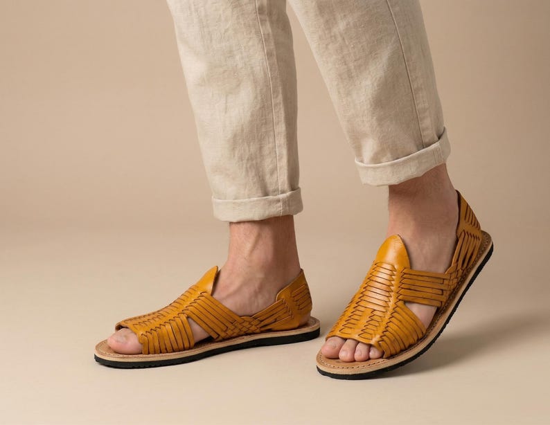 May include: Mustard yellow leather sandals with woven straps. The sandals have a black sole and a natural-coloured insole. The open-toe design and woven pattern provide a stylish and breathable footwear option.