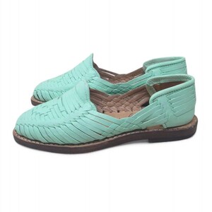 May include: A pair of mint green woven leather huarache sandals. The sandals have a flat sole and a woven design across the top. The soles are a dark brown colour. The shoes are displayed on a white background.