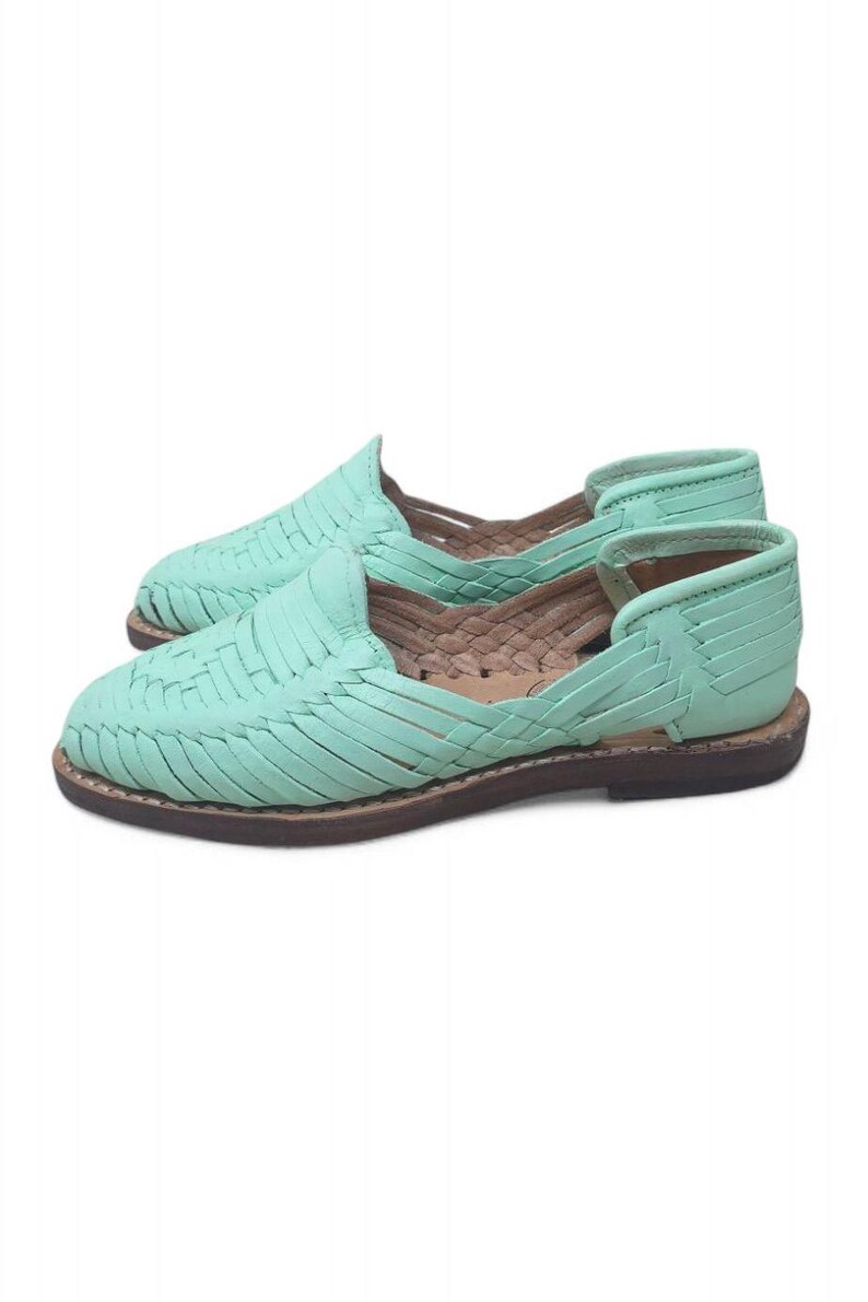 May include: A pair of mint green woven leather huarache sandals. The sandals have a flat sole and a woven design across the top. The soles are a dark brown colour. The shoes are displayed on a white background.