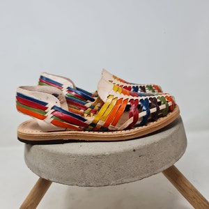 May include: A pair of colorful leather sandals with a woven design. The sandals are on a concrete pedestal with wooden legs.