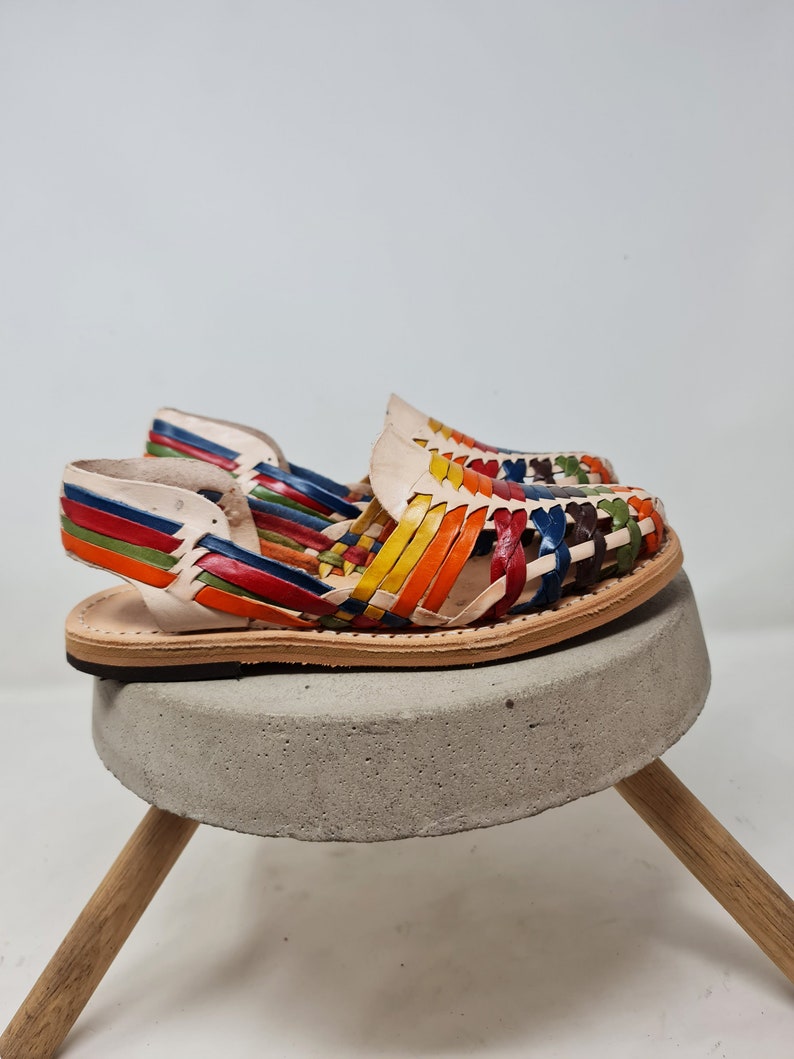 May include: A pair of colorful leather sandals with a woven design. The sandals are on a concrete pedestal with wooden legs.