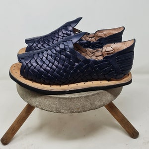 Pu&ograve; includere: Un paio di sandali in pelle blu navy con un design intrecciato. I sandali hanno una suola piatta e una punta aperta.