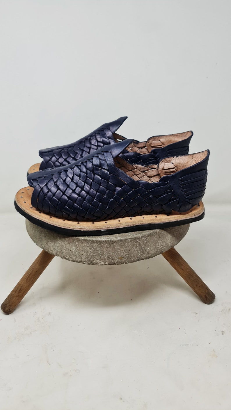 Pu&ograve; includere: Un paio di sandali in pelle blu navy con un design intrecciato. I sandali hanno una suola piatta e una punta aperta.