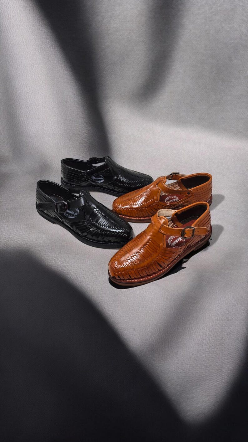 May include: Four leather sandals in black and brown. The sandals have woven uppers and buckle closures. The brown sandals are a lighter shade than the black ones. The sandals are arranged on a gray surface.
