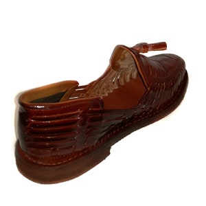 May include: A brown leather shoe with a woven design and a small tassel. The shoe has a low heel and a rounded toe. The leather has a glossy finish. The shoe is a size 9.