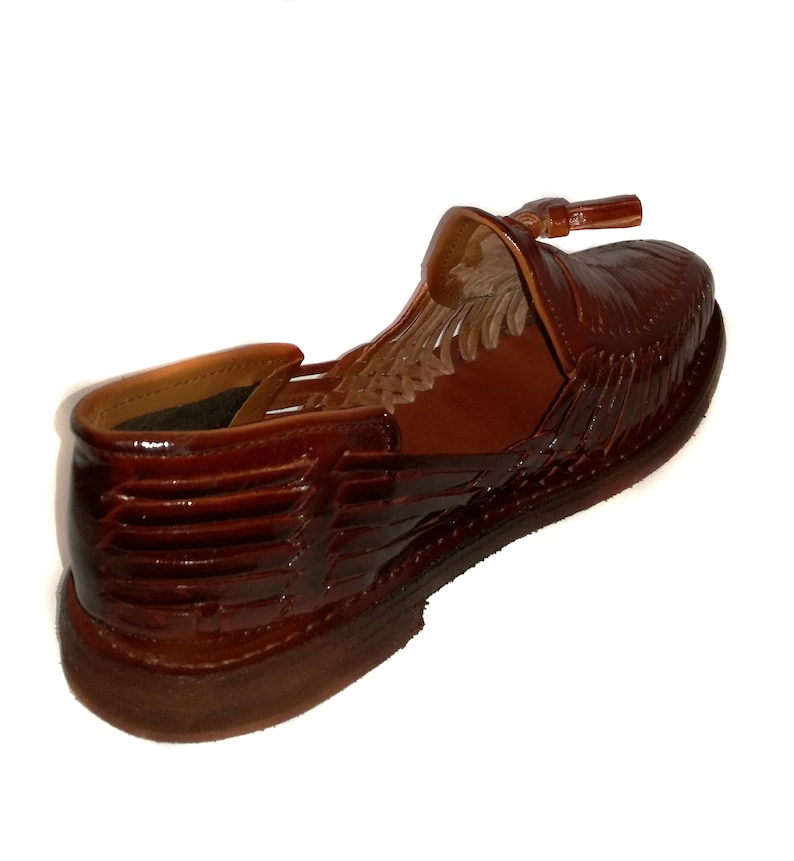 May include: A brown leather shoe with a woven design and a small tassel. The shoe has a low heel and a rounded toe. The leather has a glossy finish. The shoe is a size 9.