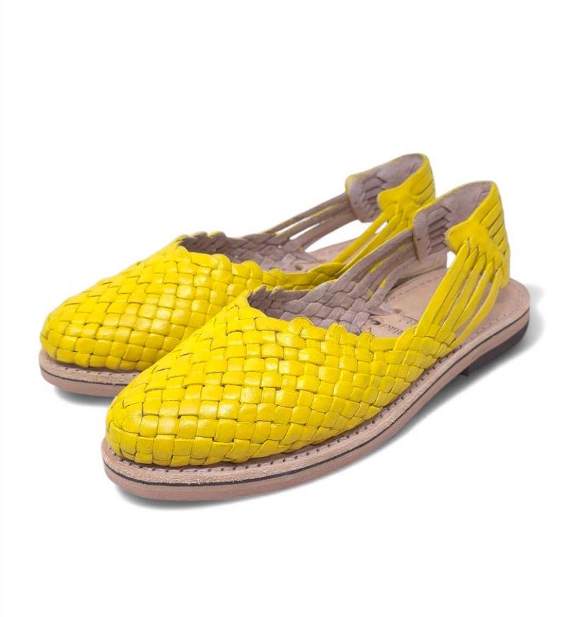 May include: A pair of yellow woven leather sandals with a simple design. The sandals have a flat sole and an open toe.