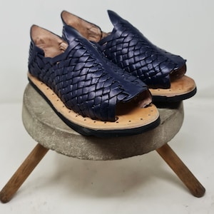 Pu&ograve; includere: Un paio di sandali in pelle blu navy con un design intrecciato. I sandali hanno una punta a punta e una suola piatta.