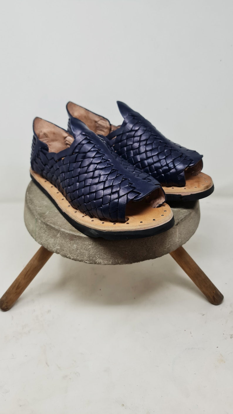 Pu&ograve; includere: Un paio di sandali in pelle blu navy con un design intrecciato. I sandali hanno una punta a punta e una suola piatta.