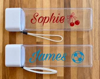 May include: Two rectangular clear plastic water bottles with white caps and white wrist straps. The top bottle features the red text Sophie and a red cherry graphic. The bottom bottle features the blue text James and a blue soccer ball graphic.