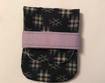 Può includere: Una piccola borsa nera con un motivo geometrico beige e bianco. La borsa ha una tracolla in tessuto lavanda.