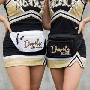 May include: Two cheerleaders wearing black and gold uniforms with matching fanny packs. One fanny pack is white with "Devils" and "Gina Marie" in gold glitter lettering. The other is black with "Devils" and "Samantha" in gold glitter lettering.