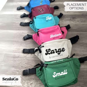 A row of colorful fanny packs with various names printed on them, placed on a wooden surface.
