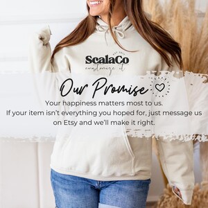 A woman wearing a white hoodie with text on it, smiling and gesturing with her hand.