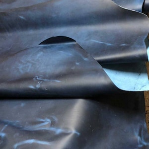 May include: A large piece of dark blue leather with a light blue marbled pattern. The leather is folded in several places, showing the texture and color variations.