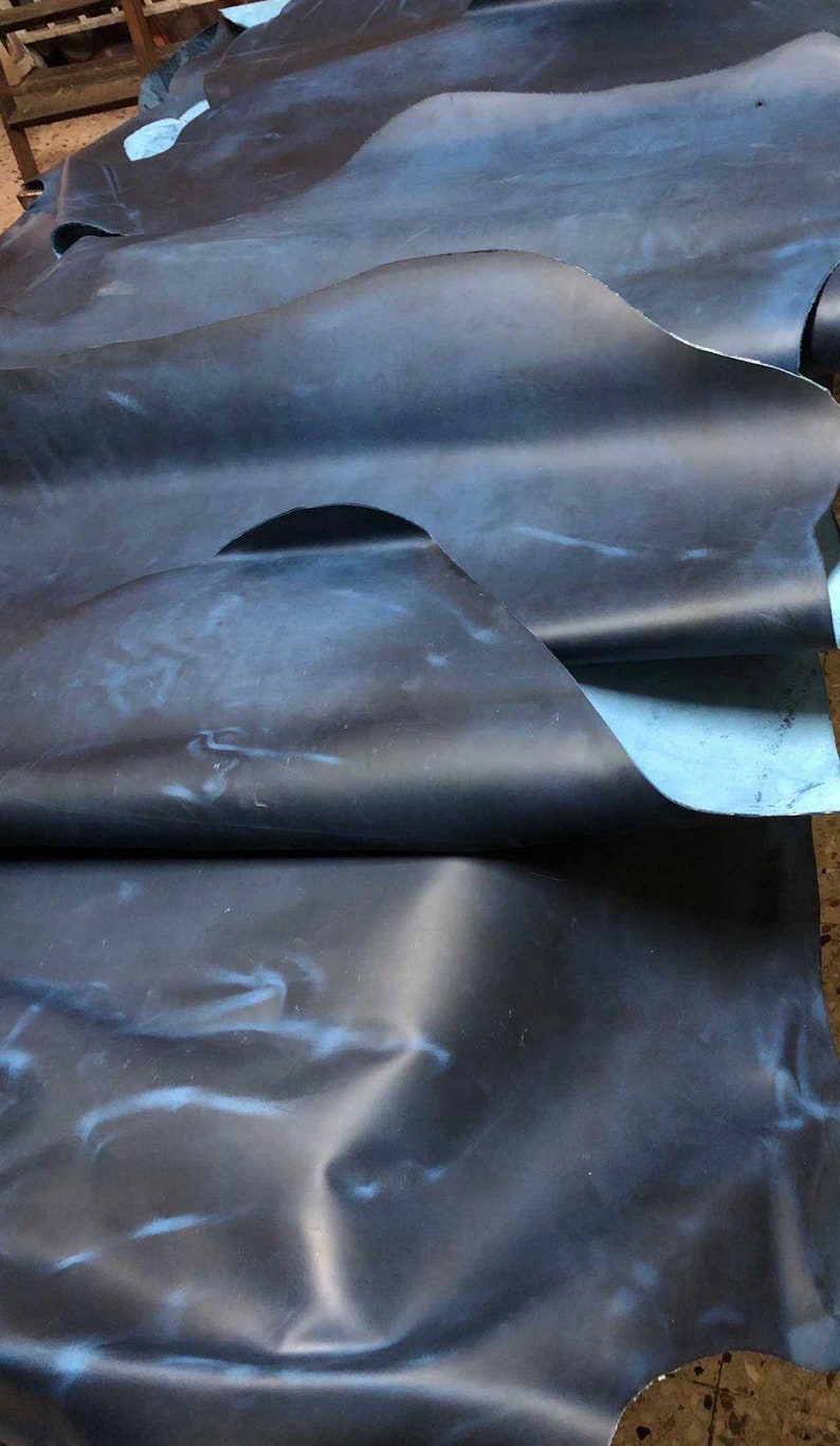 May include: A large piece of dark blue leather with a light blue marbled pattern. The leather is folded in several places, showing the texture and color variations.