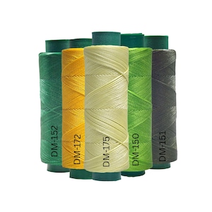Op de afbeelding: Een verzameling kleurrijke garenspoelen in groen, geel en grijs. Elke spoel is gelabeld met een code, zoals DM-152, DM-172, DM-175, DM-150 en DM-151. De draden zijn strak gewikkeld, wat een textuur geeft.