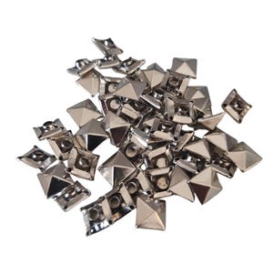 May include: A pile of silver-colored, pyramid-shaped metal studs. Each stud has a square base and a pointed top, with a small hole in the center of the base. The studs are scattered against a white background.
