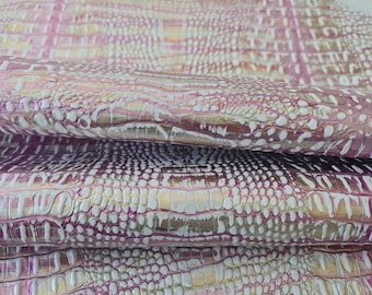May include: A close-up of a folded piece of pink and white embossed leather with a crocodile skin pattern. The leather has a metallic sheen and is textured.