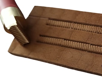 May include: A close-up of a leather working tool being used to create a rope design on a piece of brown leather.