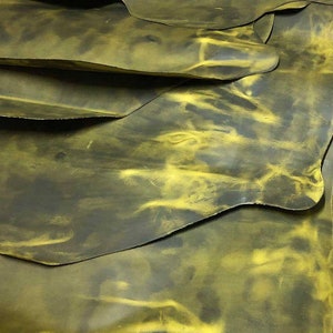 May include: Close-up of several pieces of yellow and green leather. The leather has a mottled, marbled appearance with a darker green base and lighter yellow accents.
