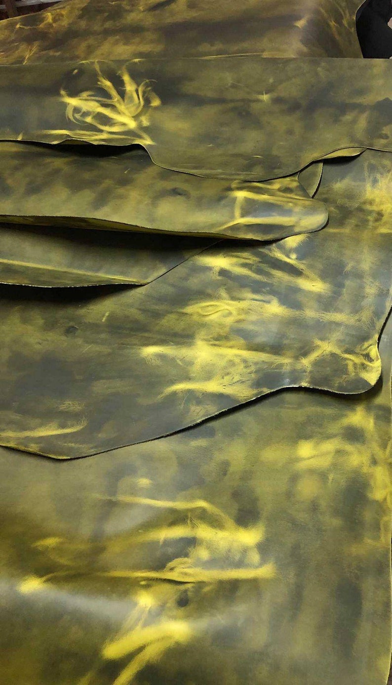 May include: Close-up of several pieces of yellow and green leather. The leather has a mottled, marbled appearance with a darker green base and lighter yellow accents.