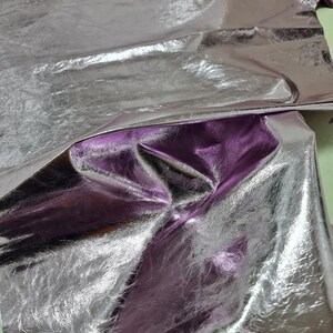 May include: A piece of silver metallic leather with a purple hue. The leather is folded and wrinkled, showing its texture.