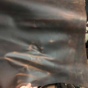 May include: A piece of brown leather with a slightly mottled appearance. The leather is folded and has a slight sheen.