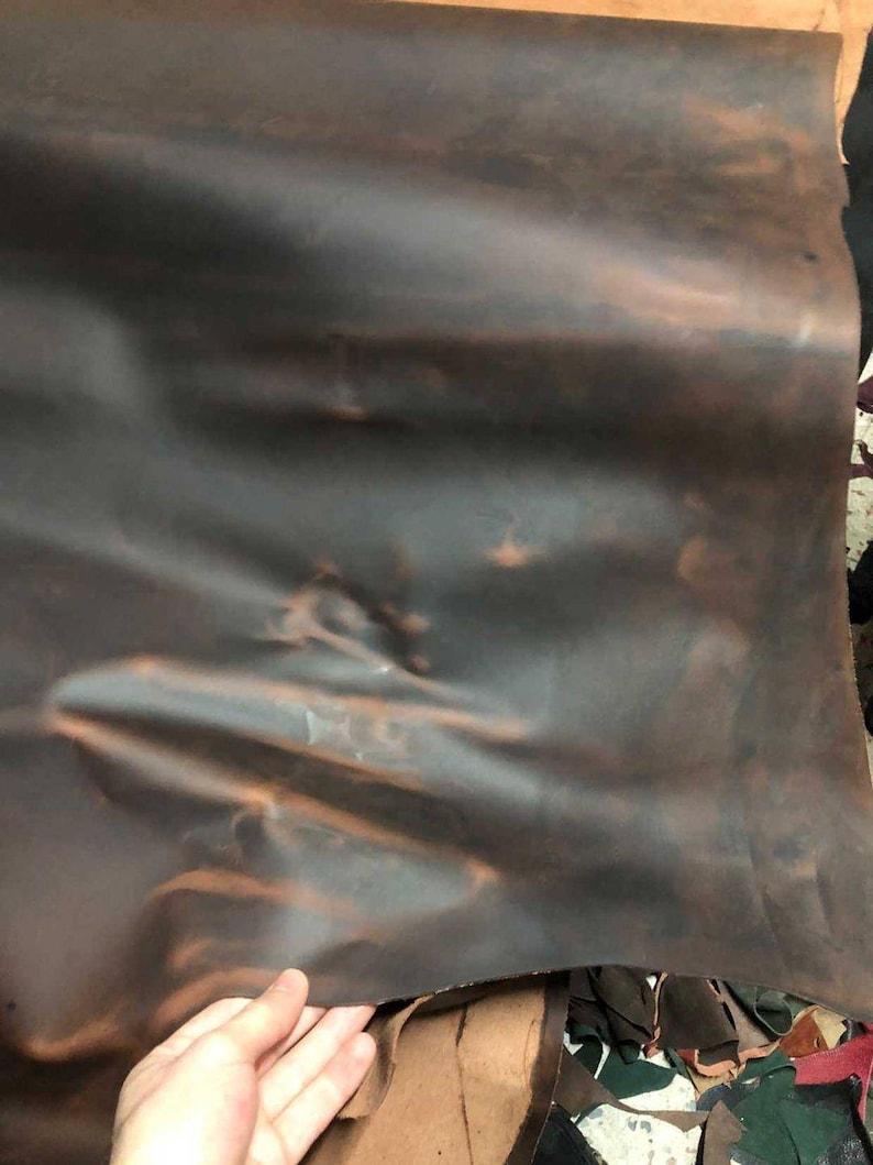 May include: A piece of brown leather with a slightly mottled appearance. The leather is folded and has a slight sheen.